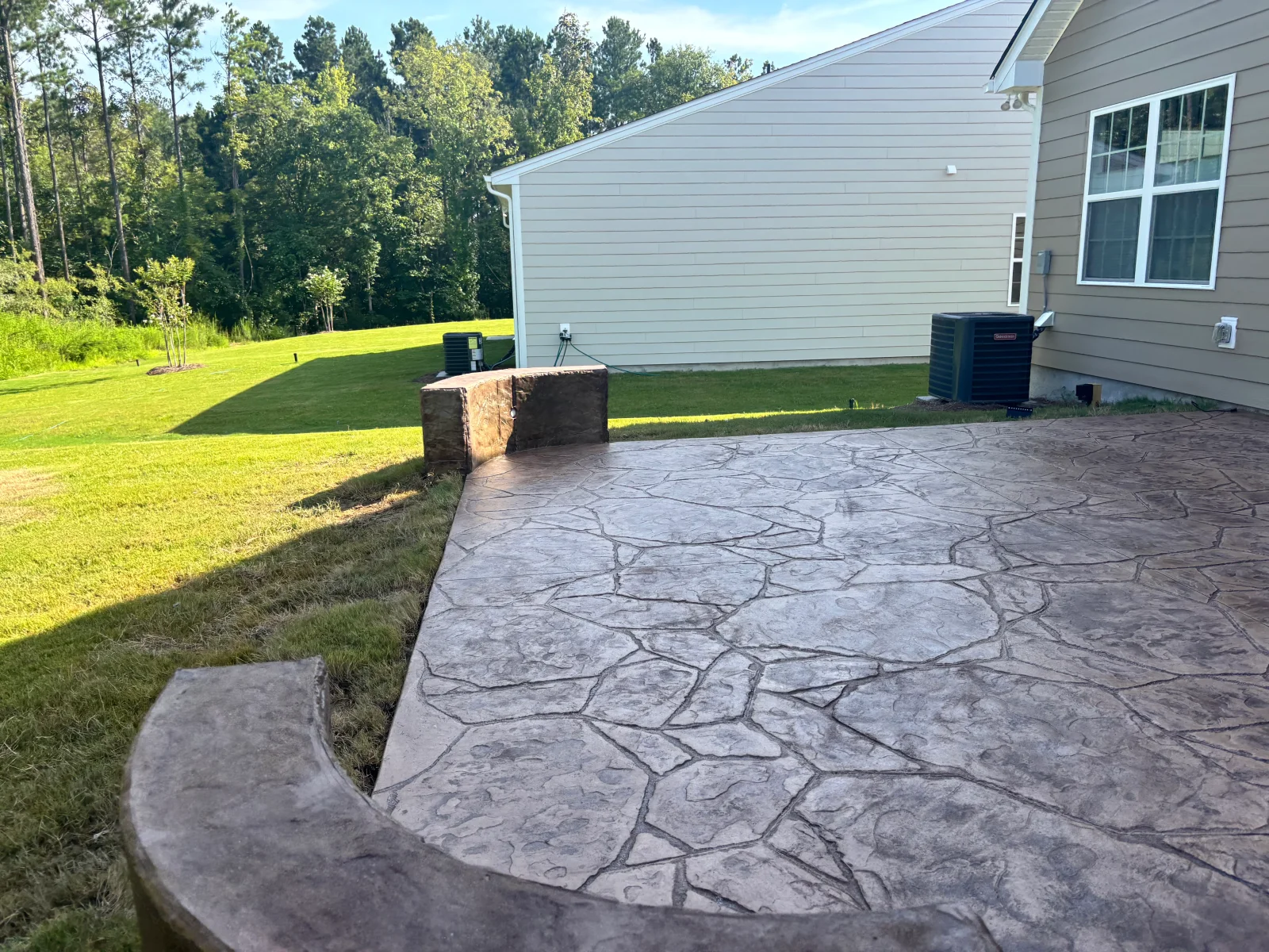 Stamped slate-pattern concrete patio with stone veneer seating wall in residential backyard