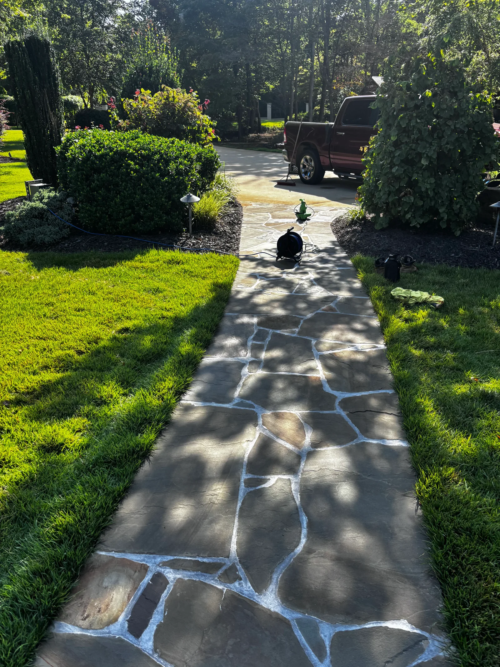 Flagstone walkway with white mortar joints bordered by green hedges and landscape lighting