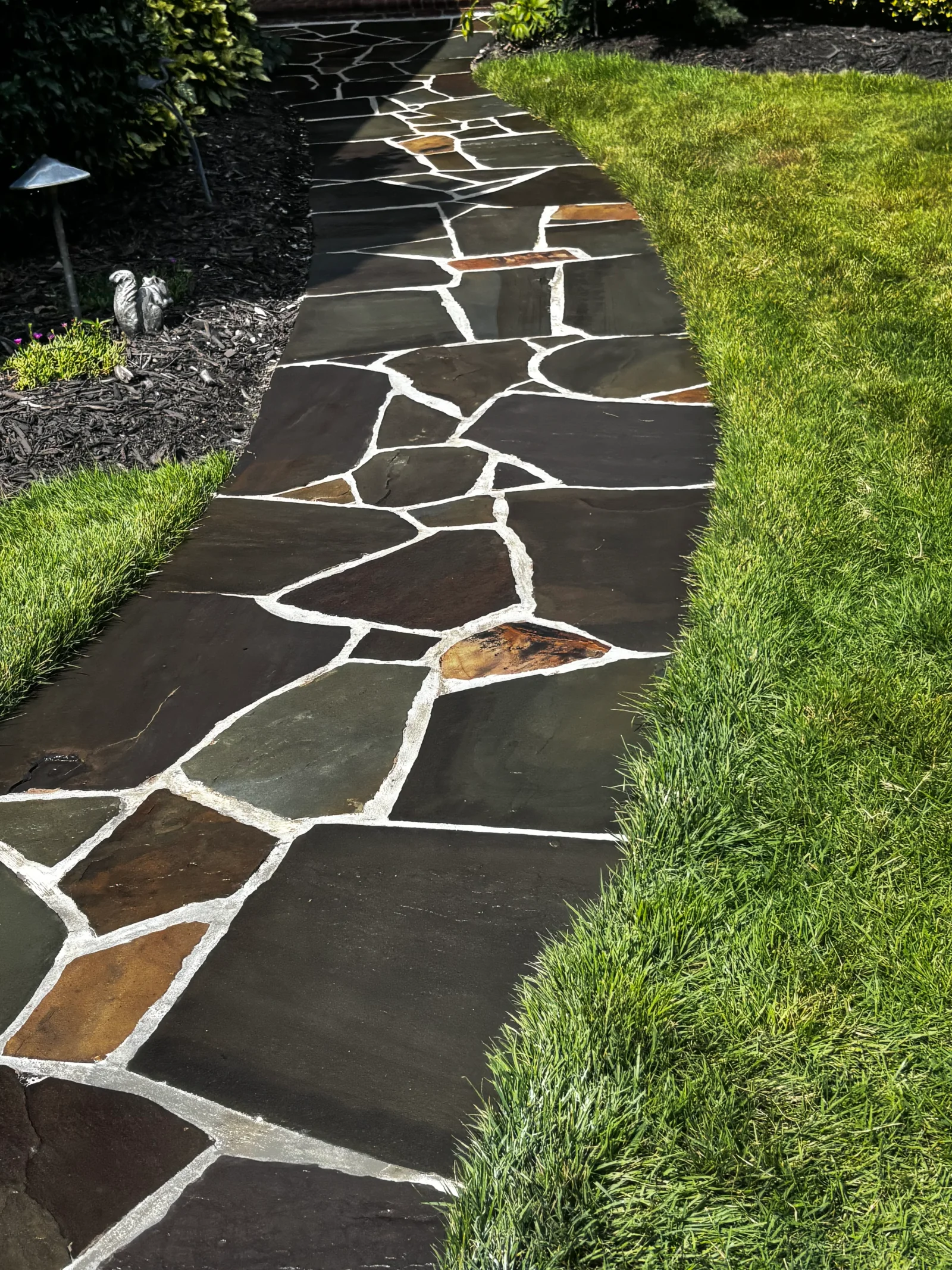 Flagstone pathway with white polymeric joints bordered by green sod and dark mulch
