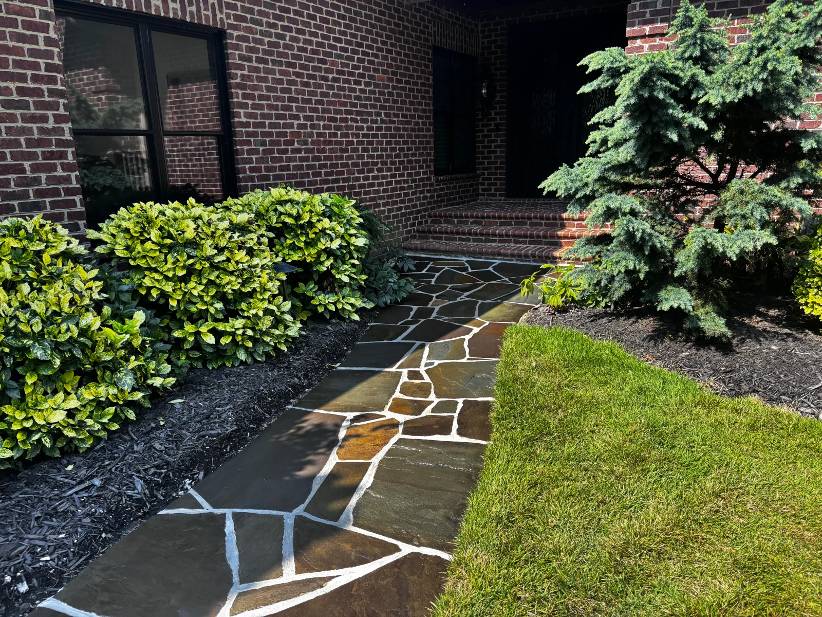 Irregular flagstone patio with white mortar joints adjacent to brick building and landscaping