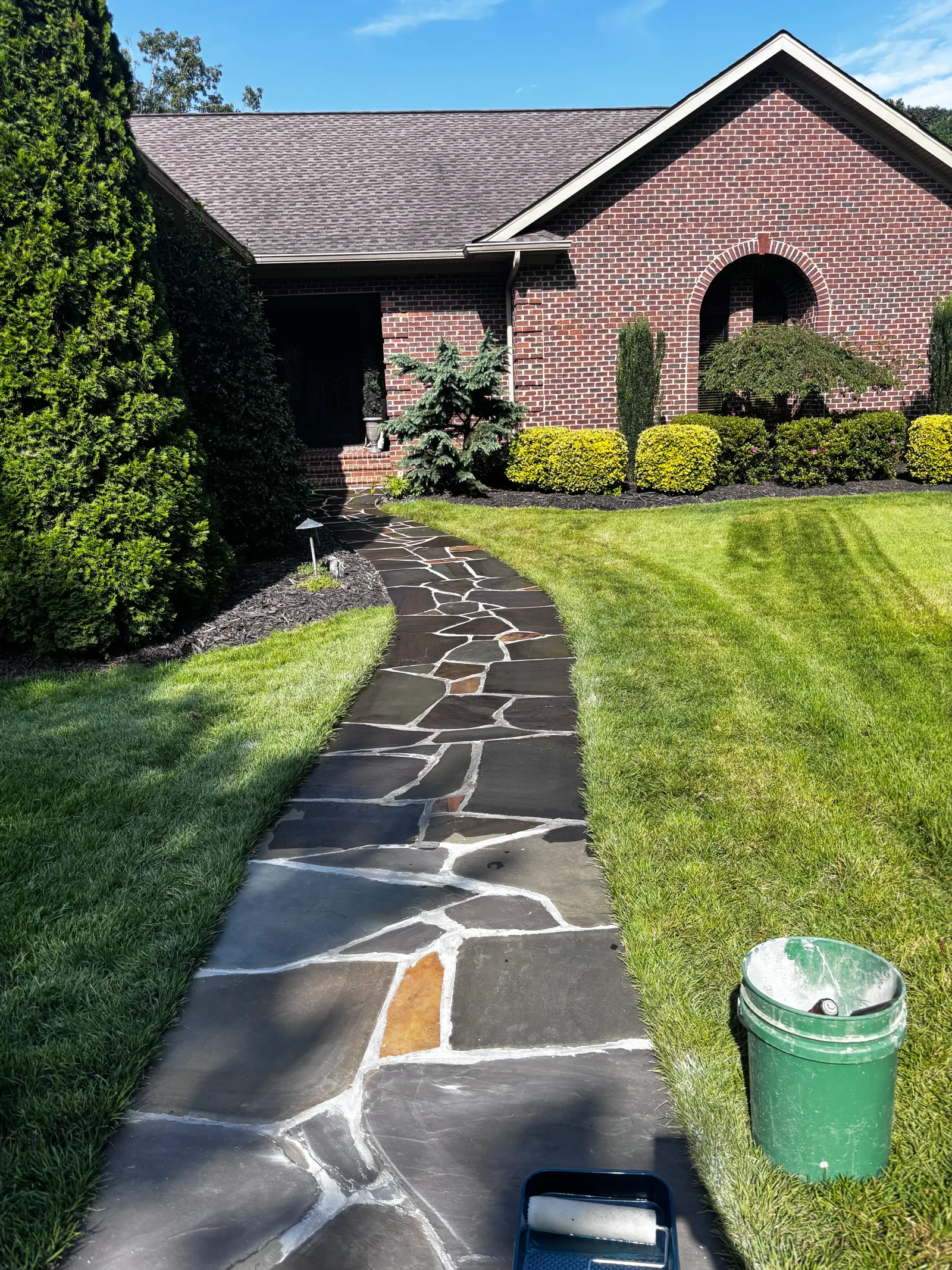 Flagstone walkway with white and colored concrete inlay pattern, bordered by manicured lawn and hedges